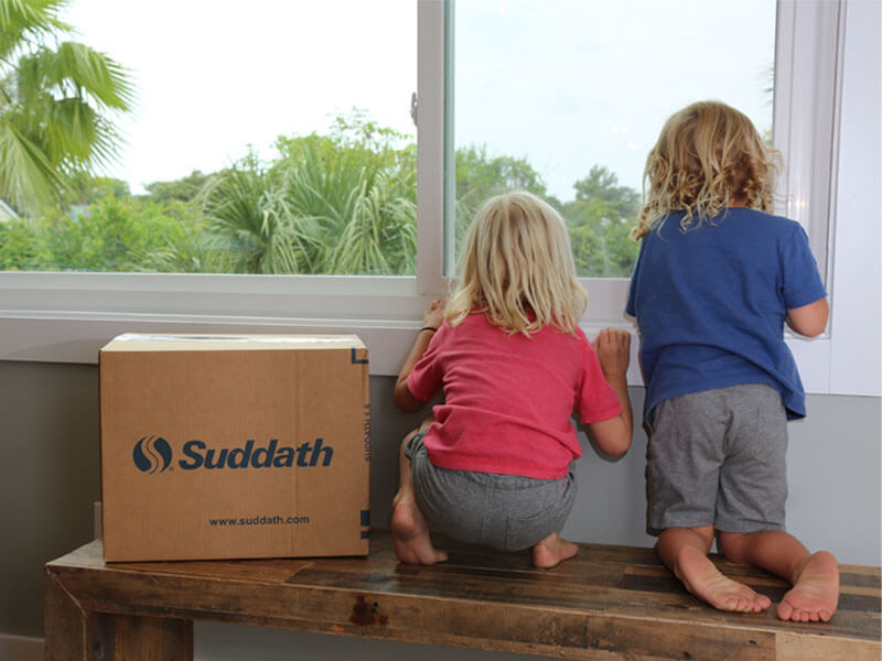 kids sitting on bench next to moving box looking out window